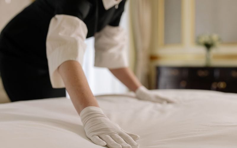 Housekeeper making bed in hotel room